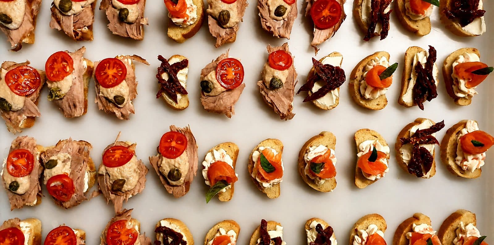 Canapés mit Tomate, Lachs und Roastbeef in Reihen, von oben fotografiert