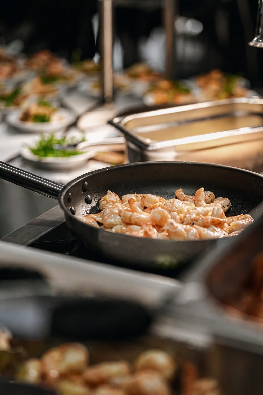 Pfanne mit Garnelen am Buffet, dahinter angerichtete Schalen