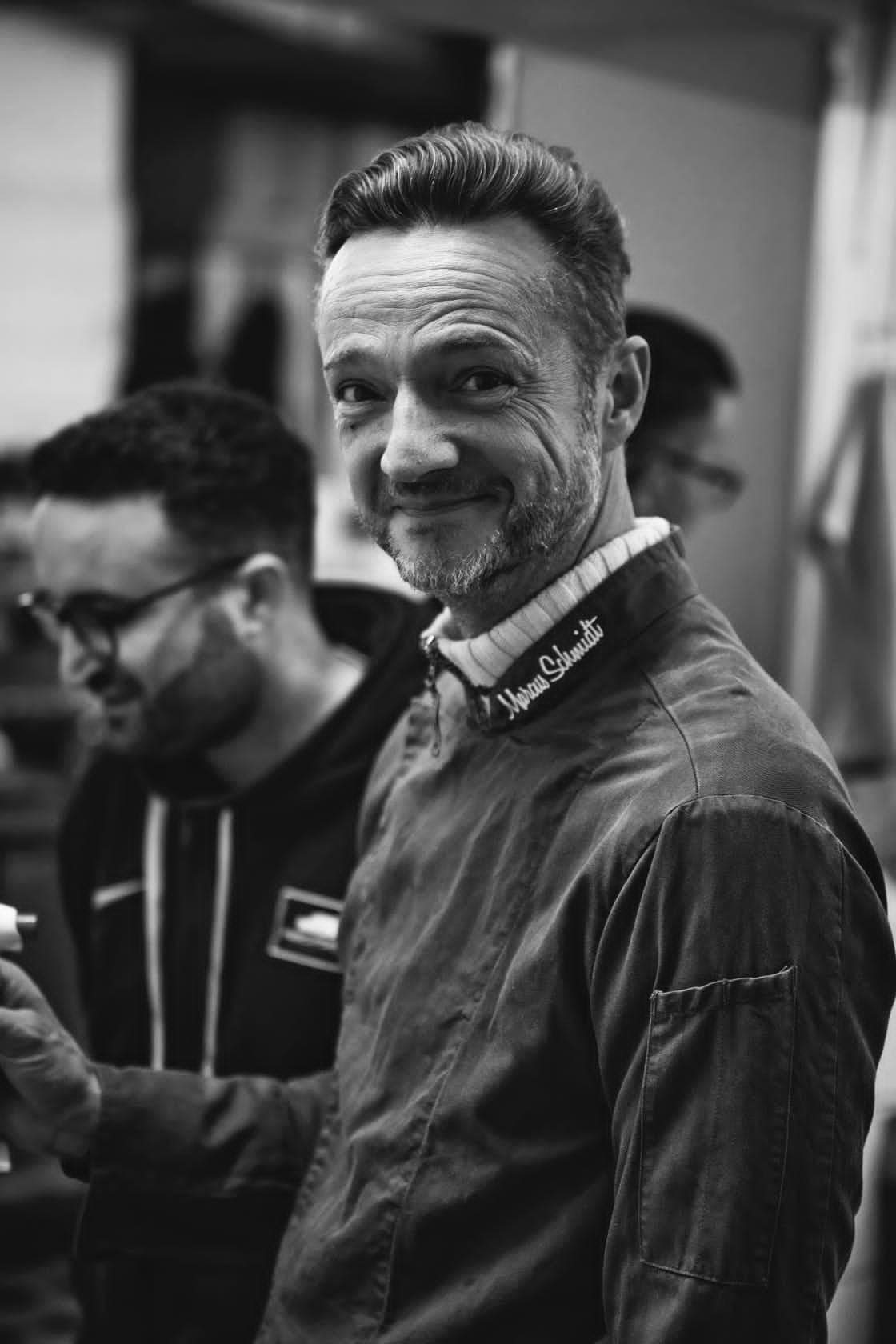 Küchenchef Marcus Schmidt lächelt in die Kamera, hinter ihm das Küchenteam