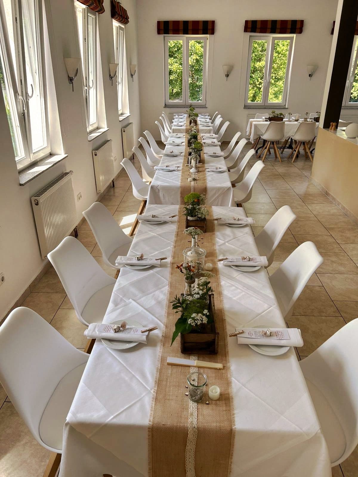 Lange Tafel mit Juteläufer, weißen Stühlen und Blumen am Fenster